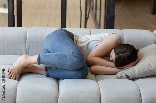 Unhappy depressed young woman sleeping on couch at home, feeling unwell and unhealthy, frustrated upset female lying on couch, crying, suffering from divorce or break up, psychological problem