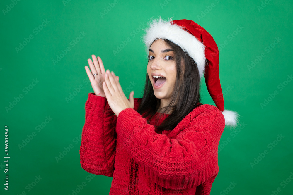 Young beautiful woman wearing Christmas Santa hat over isolated green background clapping and applauding happy and joyful, smiling proud hands together Young beautiful woman wearing Christmas Santa hat over isolated green background clapping and applauding happy and joyful, smiling proud hands together