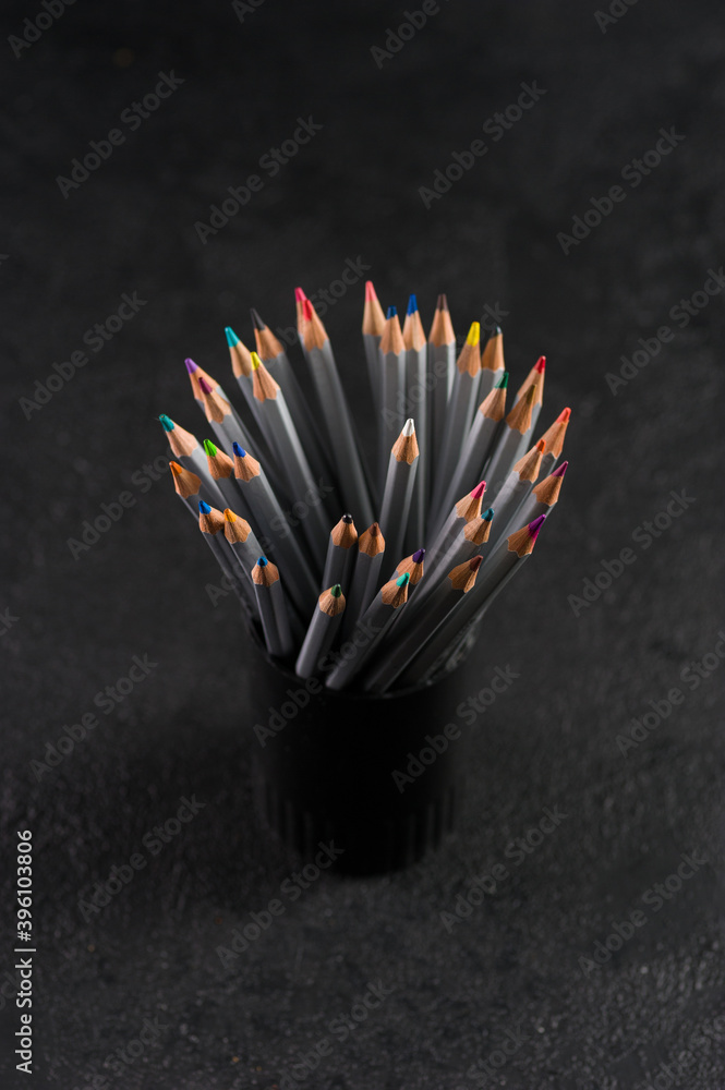 stylish set of colored pencils for creativity, in a black plastic cup on a gray background with a place for text, vertical format