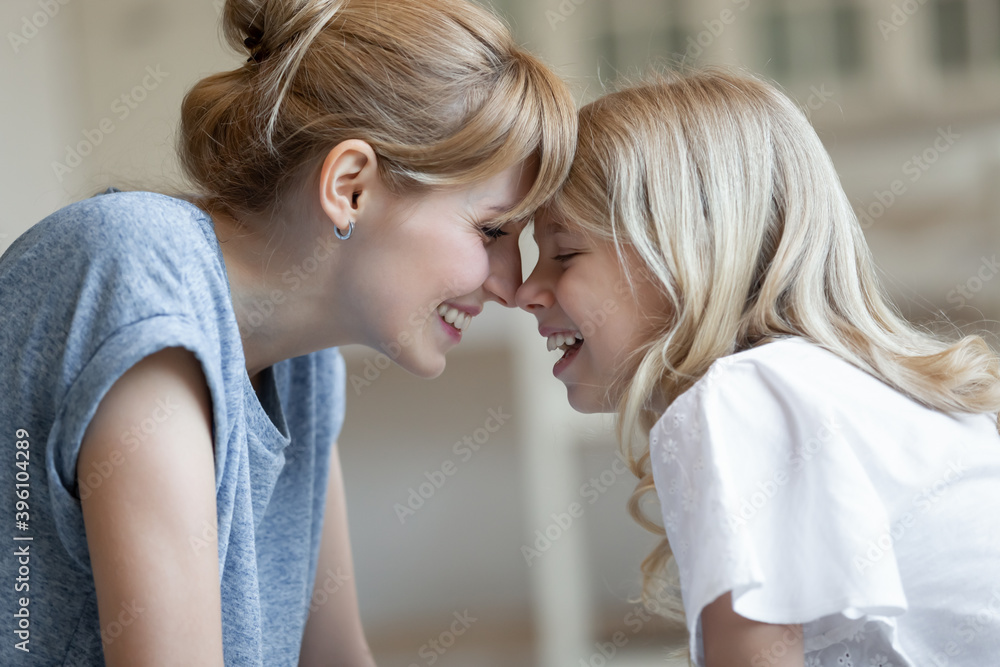 Fototapeta premium Close up side view happy laughing mother and little daughter touching foreheads, enjoying tender moment, overjoyed beautiful young mum and adorable child cuddling, good family relationship