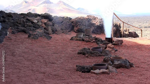 Man pouring bucket of water into geyser and steam erupts abruptly in Timanfaya National Park. Tourist attraction, geothermal phenomenom concepts