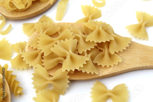 Pasta in the form of bows lie on a wooden spoon on a white background