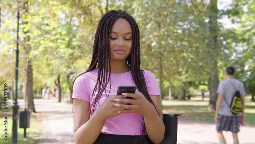 A young black woman works on a smartphone in a park on a sunny day A young black woman works on a smartphone in a park on a sunny day