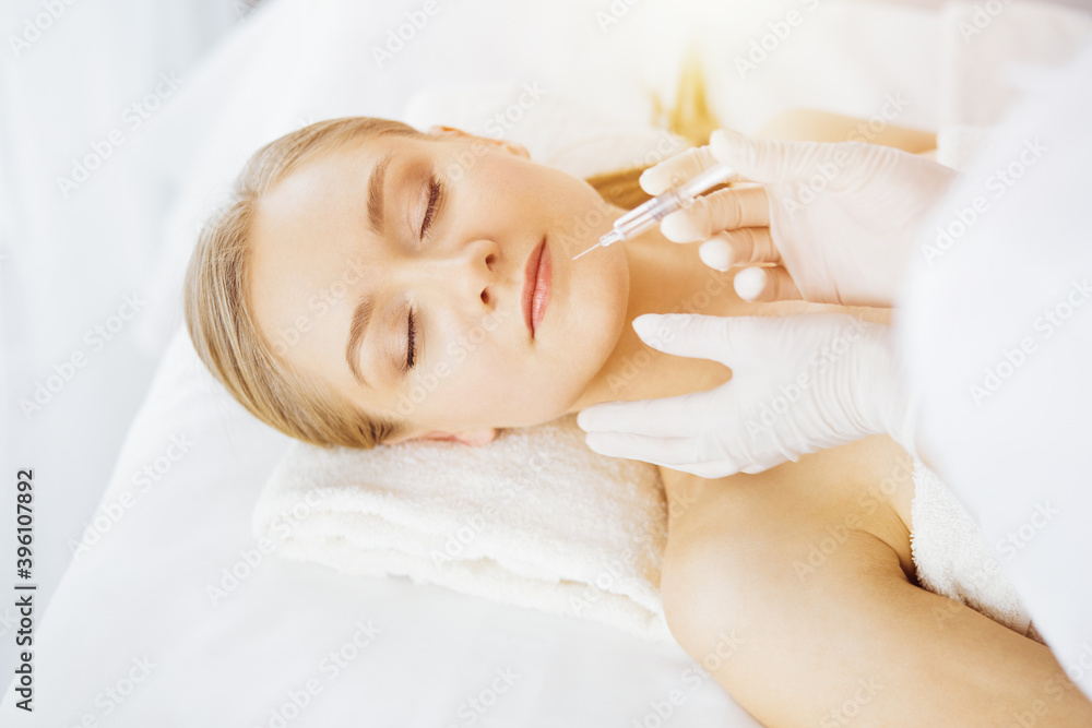 Beautician doctor doing beauty procedure with syringe to caucasian female face in synny room. Cosmetic medicine and surgery, beauty injections concept Beautician doctor doing beauty procedure with syringe to caucasian female face in synny room. Cosmetic medicine and surgery, beauty injections concept