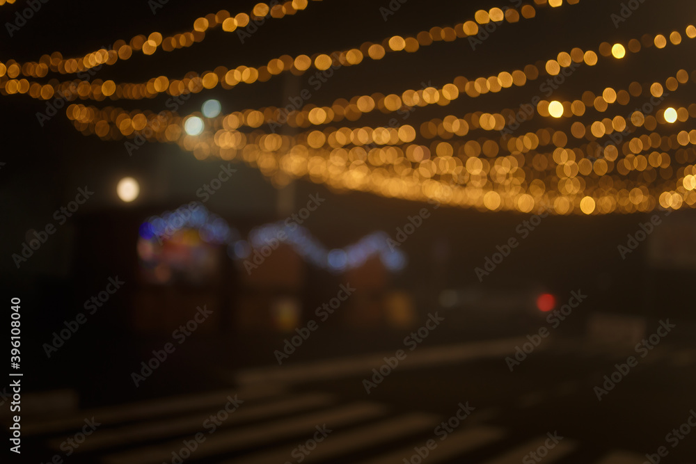 Unfocused night shot of Christmas garland lights bokeh in the city. Happy New Year, Merry Christmas, winter holidays concept.