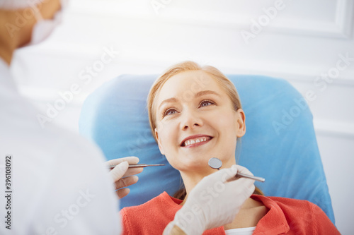 Smiling caucasian woman is being examined by dentist at sunny dental clinic. Healthy teeth and medicine, stomatology concept