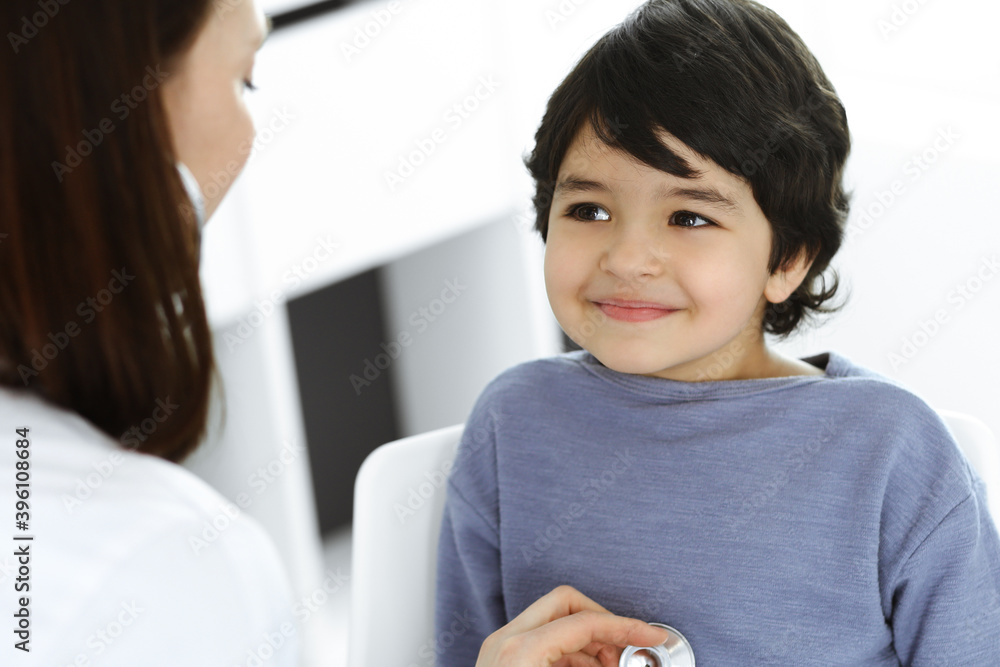 Doctor-woman examining a child patient by stethoscope. Cute arab boy at physician appointment. Medicine concept Doctor-woman examining a child patient by stethoscope. Cute arab boy at physician appointment. Medicine concept