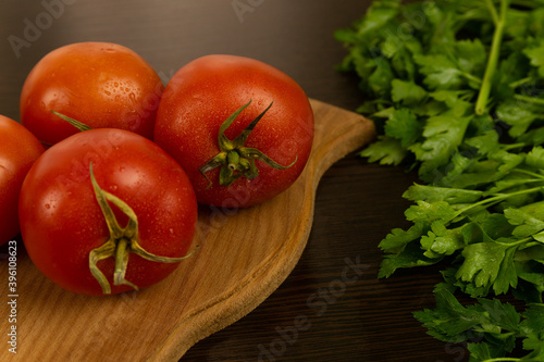 Red tomatoes on a wooden board and a dark textured wood background. With herbs. Eco-friendly tomatoes. Fresh tomatoes. Tomatoes with water drops