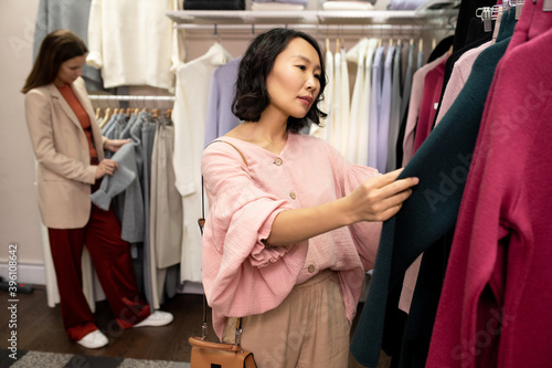 Young Asian female customer in pink smart blouse looking for new sweater © pressmaster