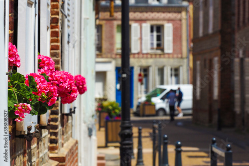 Beautiful view of scenic medieval old street of Normandy, with historic traditional houses, cobbled street in an old town in Europe. Pink flowers of geranium in pot on the window