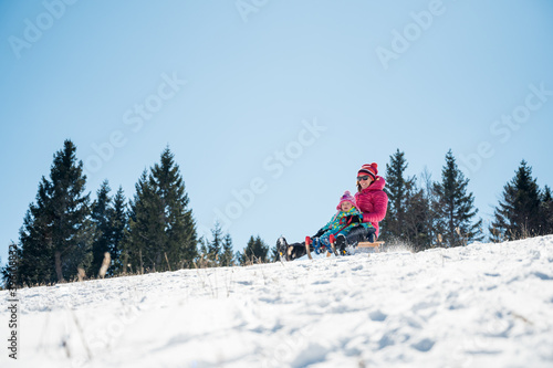 Mother and daughter sledging across fresh snow covered slopes.
