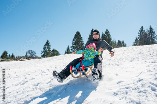 Father and daughter sledging across fresh snow covered slopes.