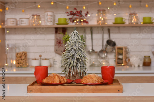 Fresh croissants on a plate, cups, Christmas tree on the background of Christmas kitchen.