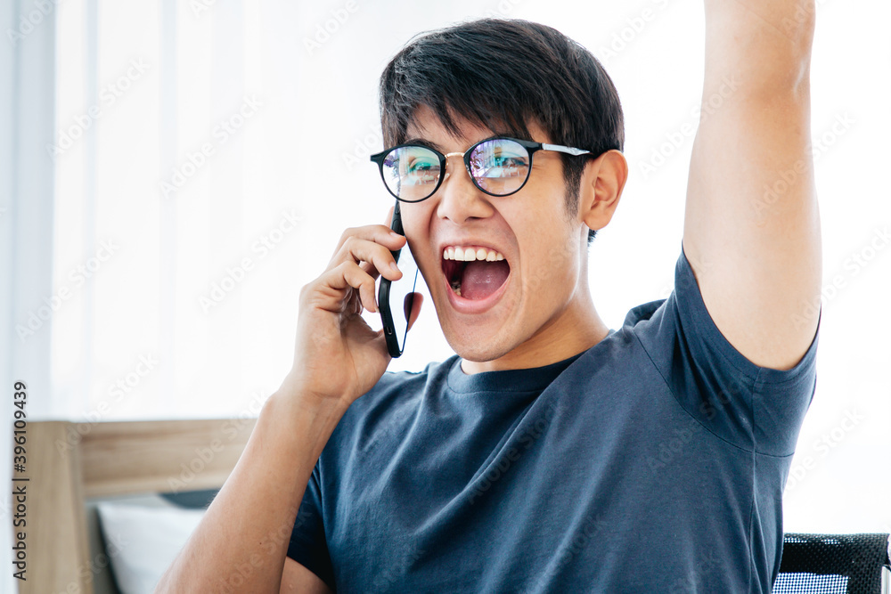 Close up Surprised happy Asian man using mobile phone on desk read good news on internet, amazed Asian guy winner excited win scream with joy celebrate victory success at home.  With Copy Space.