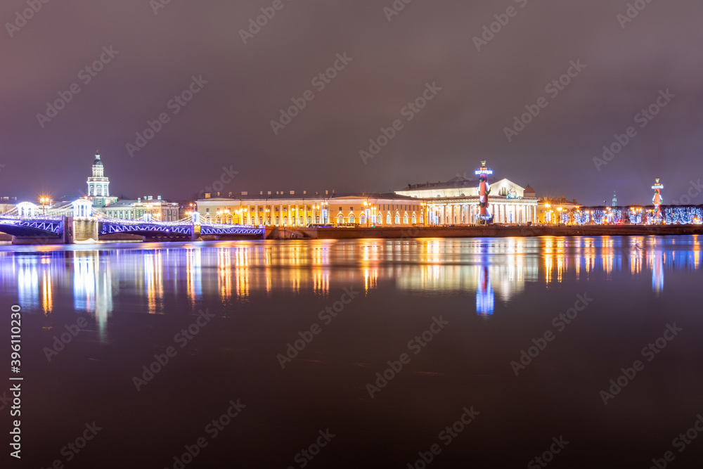 Fototapeta premium Spit (Strelka) of Vasilyevsky island with Rostral columns, Kunstkamera museum and Palace bridge at night during New Year and Christmas holidays, Saint Petersburg, Russia