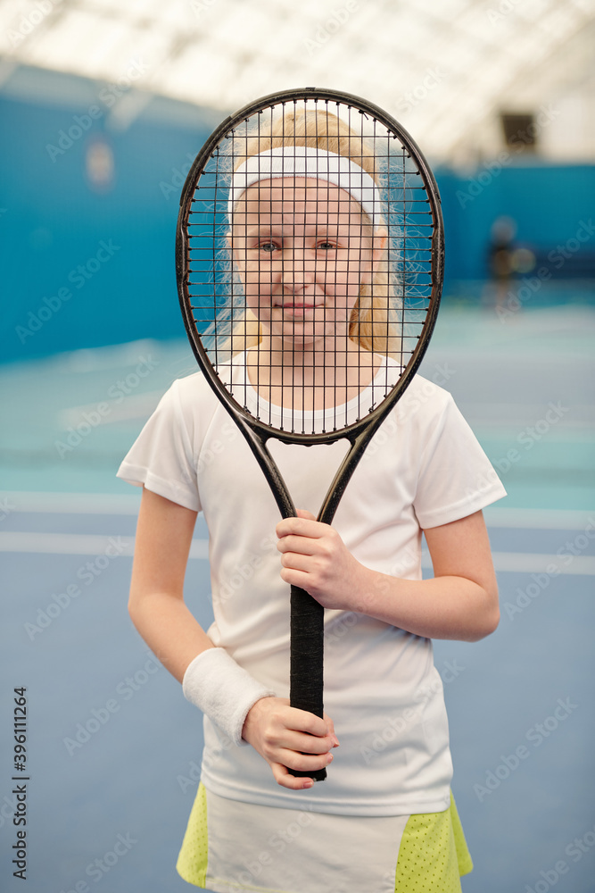 Pretty blond girl in white activewear holding tennis racket in front of her face