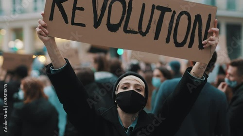 Revoultion concept. Young woman with face mask and banner protesing in the crowd. High quality 4k footage photo