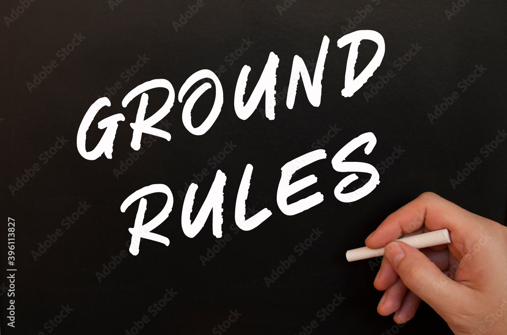 Male hand writes in chalk the words GROUND RULES on a black board. Male hand writes in chalk the words GROUND RULES on a black board.