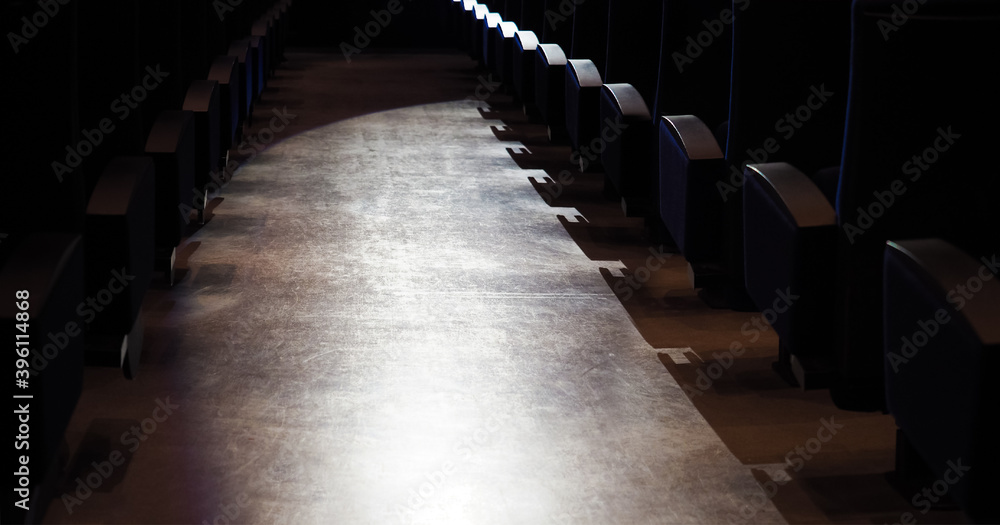 Rows of armchairs in a theater or cinema, panoramic back view. Concert seats in dark theater, light spotlight between rows. Empty theater
