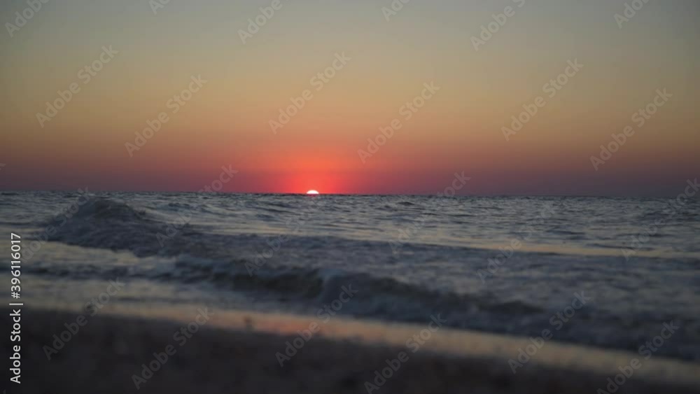 Calm picture of a sea sunset. The red sun sets in the sea. Incoming waves. The sky is colored red Calm picture of a sea sunset. The red sun sets in the sea. Incoming waves. The sky is colored red