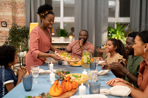 Young African woman putting appetizing homemade sandwiches on festive table