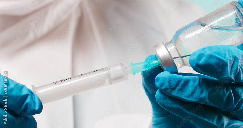 Infectious doctor or nurse in latex blue rubber gloves holds a syringe and Covid-19 coronavirus vaccine vial Infectious doctor or nurse in latex blue rubber gloves holds a syringe and Covid-19 coronavirus vaccine vial