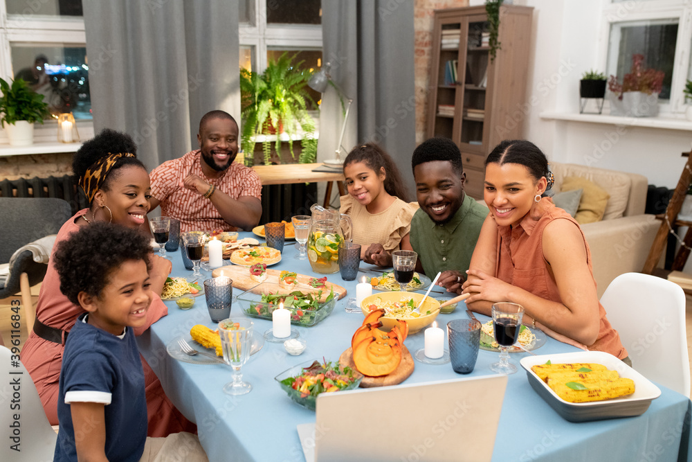 Happy African family talking to their friends in video chat by festive table Happy African family talking to their friends in video chat by festive table