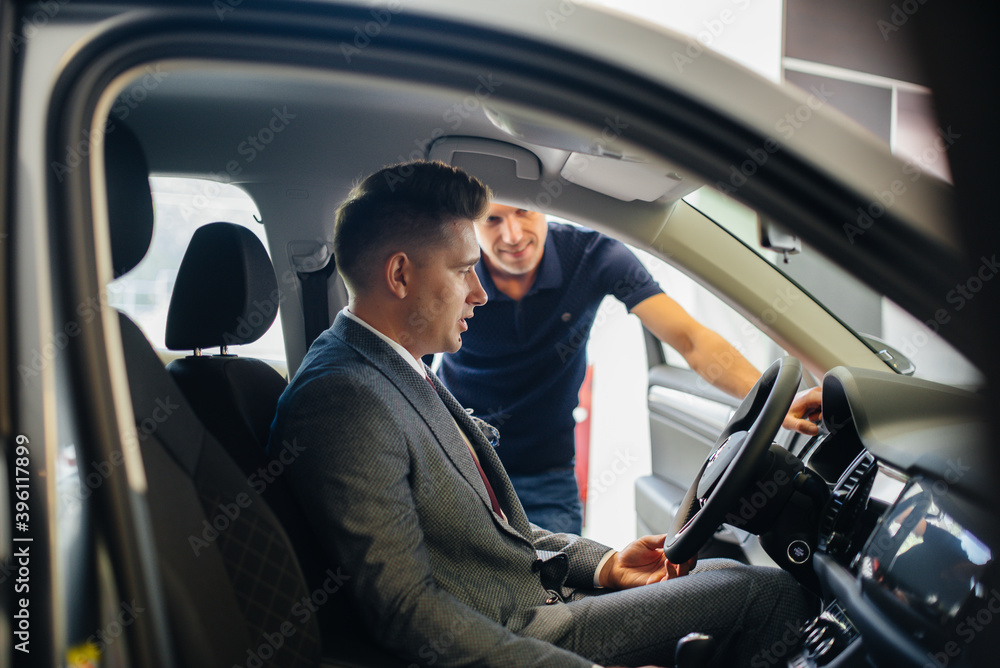 A young businessman with a salesman looks at a new car in a car dealership. Buying a car A young businessman with a salesman looks at a new car in a car dealership. Buying a car