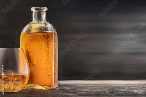 a bottle and a steamed glass with alcohol whiskey or Bourbon Scotch on the table, drops on the glass dark wooden background. copy space