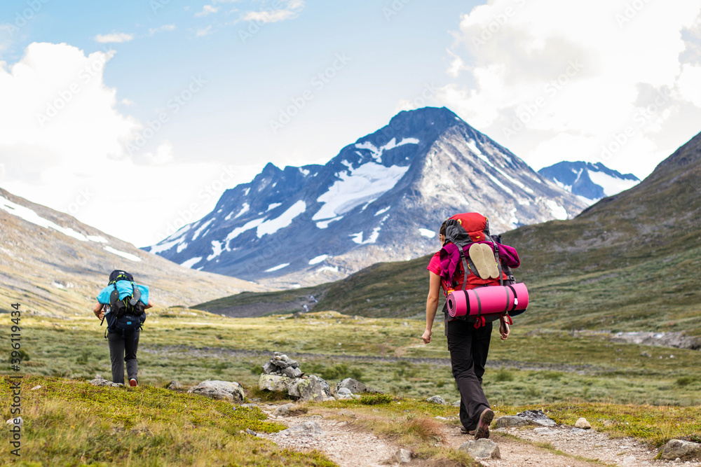 Rear view shot of two female hikers going through grass trail with awesome view to snowy mountains in Norway