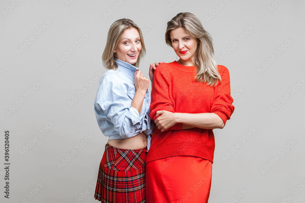 Best friends. Portrait of two fashion female models in stylish casual clothes standing together, smiling at camera. women showing autumn trends. indoor studio shot isolated on gray background Best friends. Portrait of two fashion female models in stylish casual clothes standing together, smiling at camera. women showing autumn trends. indoor studio shot isolated on gray background