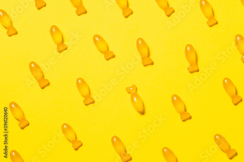 Seamless pattern with fish-shaped cod liver oil capsules on bright yellow background. Healthy lifestyle concept. Omega 3 fish oil capsules with vitamin D for children.