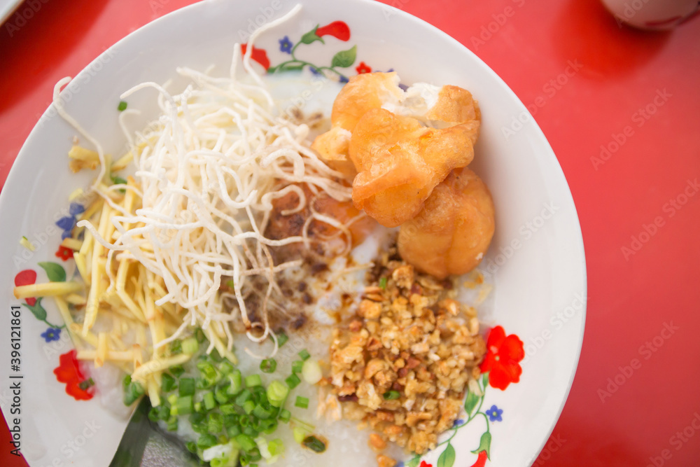 Pork rice porridge with soft-boiled egg, deep-fried dough stick, sliced ginger, spring onion and fried garlic served with hot chinese tea at local morning market. Pork rice porridge with soft-boiled egg, deep-fried dough stick, sliced ginger, spring onion and fried garlic served with hot chinese tea at local morning market.