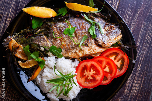Fried gilthead with juicy fresh lemon and rice garnish and tomatoes close-up