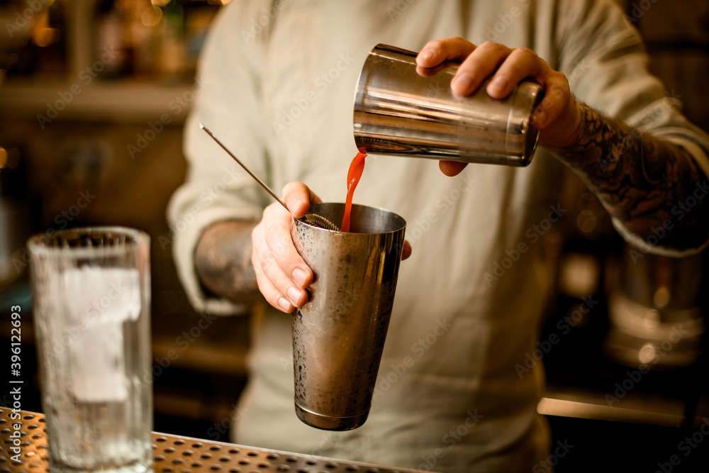 bartender pours tomato juice from one steel shaker glass into another glass