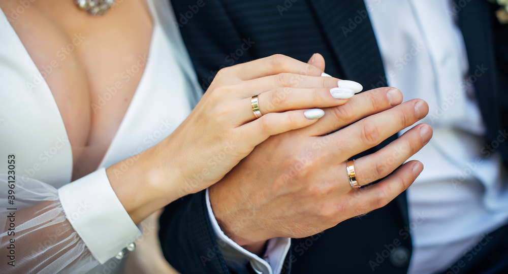 Hands of the bride and groom close-up, blurred background. Gold wedding rings on the fingers of newlyweds. Concept of marriage.