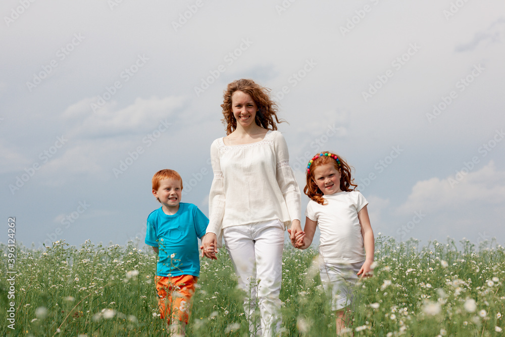 Redhead kids having fun with mom in green grass on background of blue sky Redhead kids having fun with mom in green grass on background of blue sky
