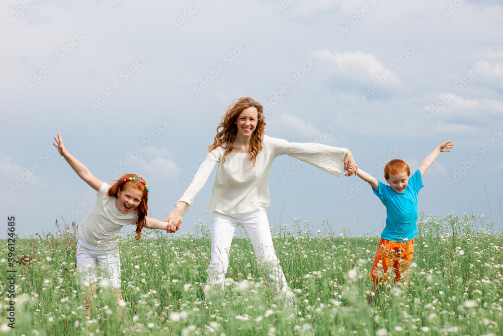 Redhead kids having fun with mom in green grass on background of blue sky Redhead kids having fun with mom in green grass on background of blue sky