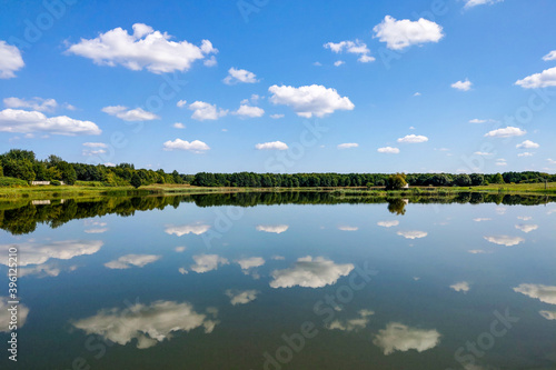 Beautiful landscape, reflection in clear water. Lake against the blue sky with white fluffy clouds. © Dzmitry