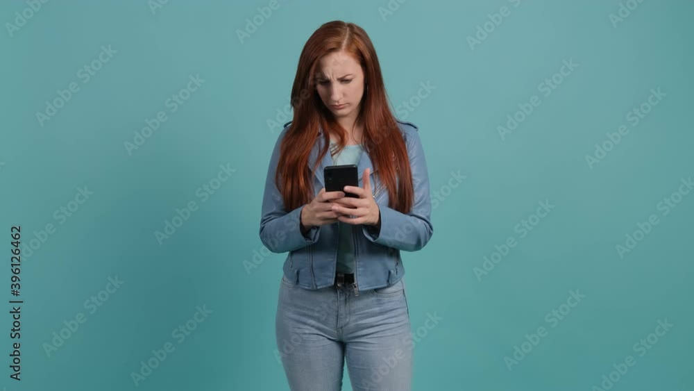 Portrait of a upset confused woman looking at mobile phone isolated over turquoise background. Portrait of a upset confused woman looking at mobile phone isolated over turquoise background.