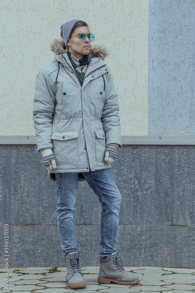 A man in winter clothes stands against the background of the wall in full growth and looks thoughtfully into the distance A man in winter clothes stands against the background of the wall in full growth and looks thoughtfully into the distance
