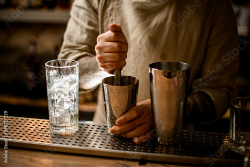 Foto bartender prepares cocktail in shaker cup using the muddler