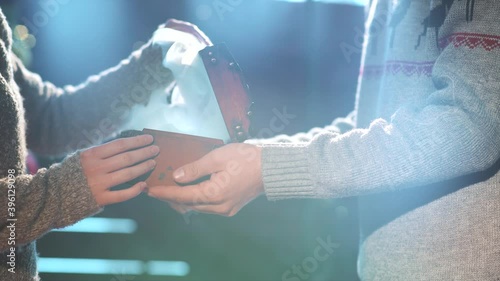 Man presenting a xmas gift to a woman. Close up of hands present a cascet with faity light and smoke on garland bokeh background. Merry christmas and happy new year concept. Celebrating holidays photo