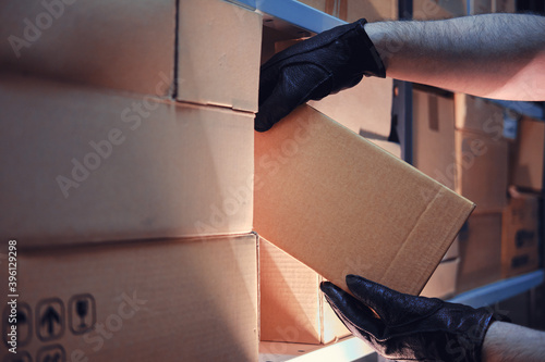 Hands of a man in leather gloves take a box of goods in a warehouse at night. Concept of security problems in warehouses and stores photo