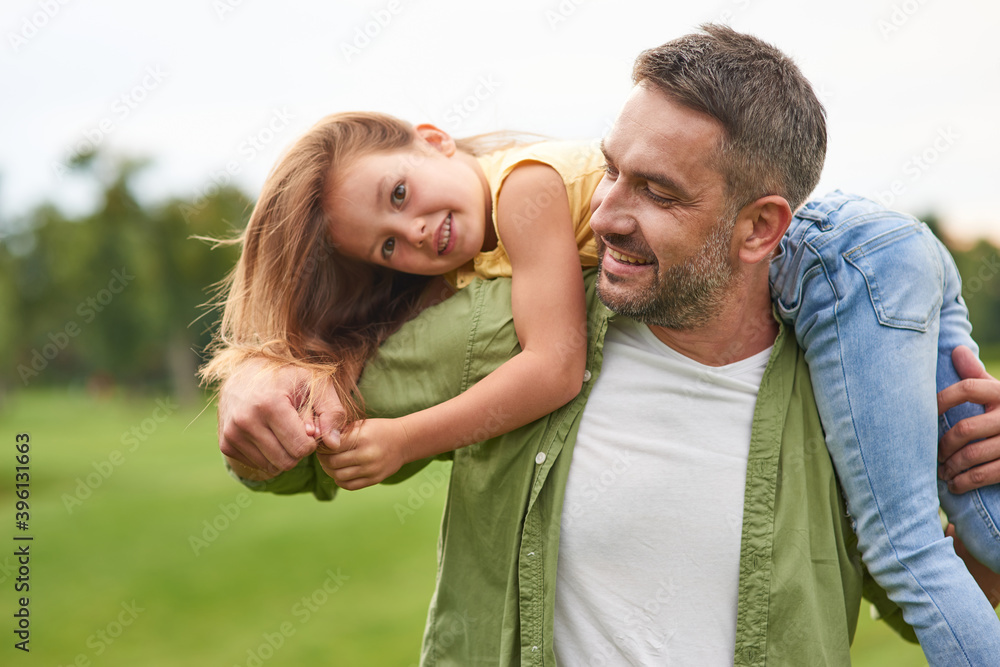 Fototapeta premium Happy father playing with his cute little daughter, holding her on his shoulders and smiling, daughter and daddy spending time together outdoors