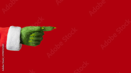 A green hairy hand in a Santa suit points to the right on a red background photo