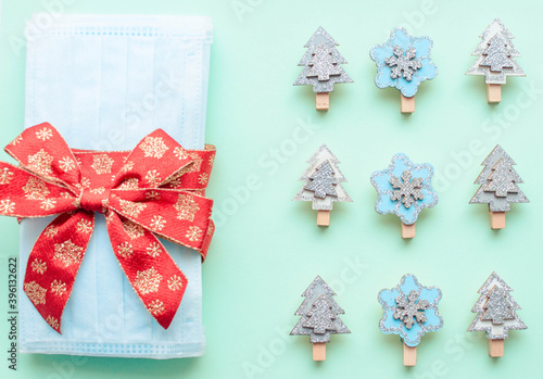 medical protective face masks as a gift with a red ribbon on a green background. Christmas and New Year 2021 decor painted firs and snowflakes. Holidays self-isolation and coronavirus pandemic concept
