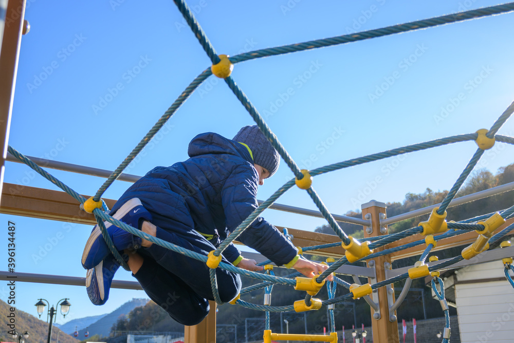 Little boy climbing on rope in playground at sunny autumn day