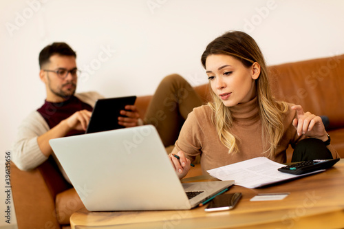 Young woman using laptop and young man using digital tablet while sitting on sofa at home