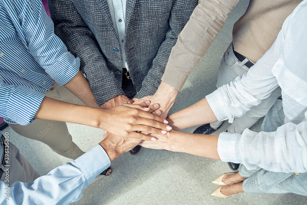 Close up shot of business people putting hands together and smiling, celebrating success while standing at office